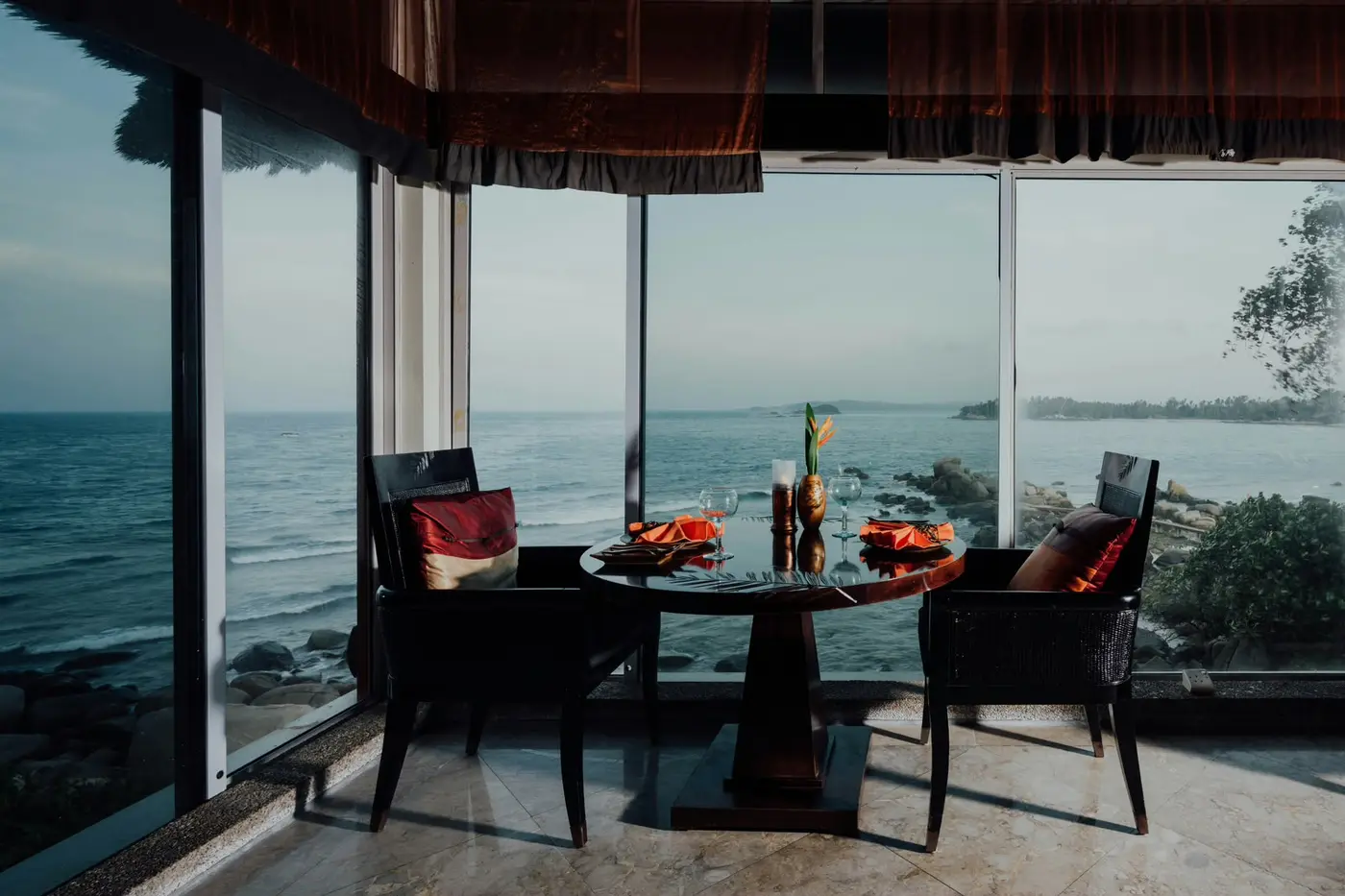 Table set for two beside panoramic windows overlooking the sea